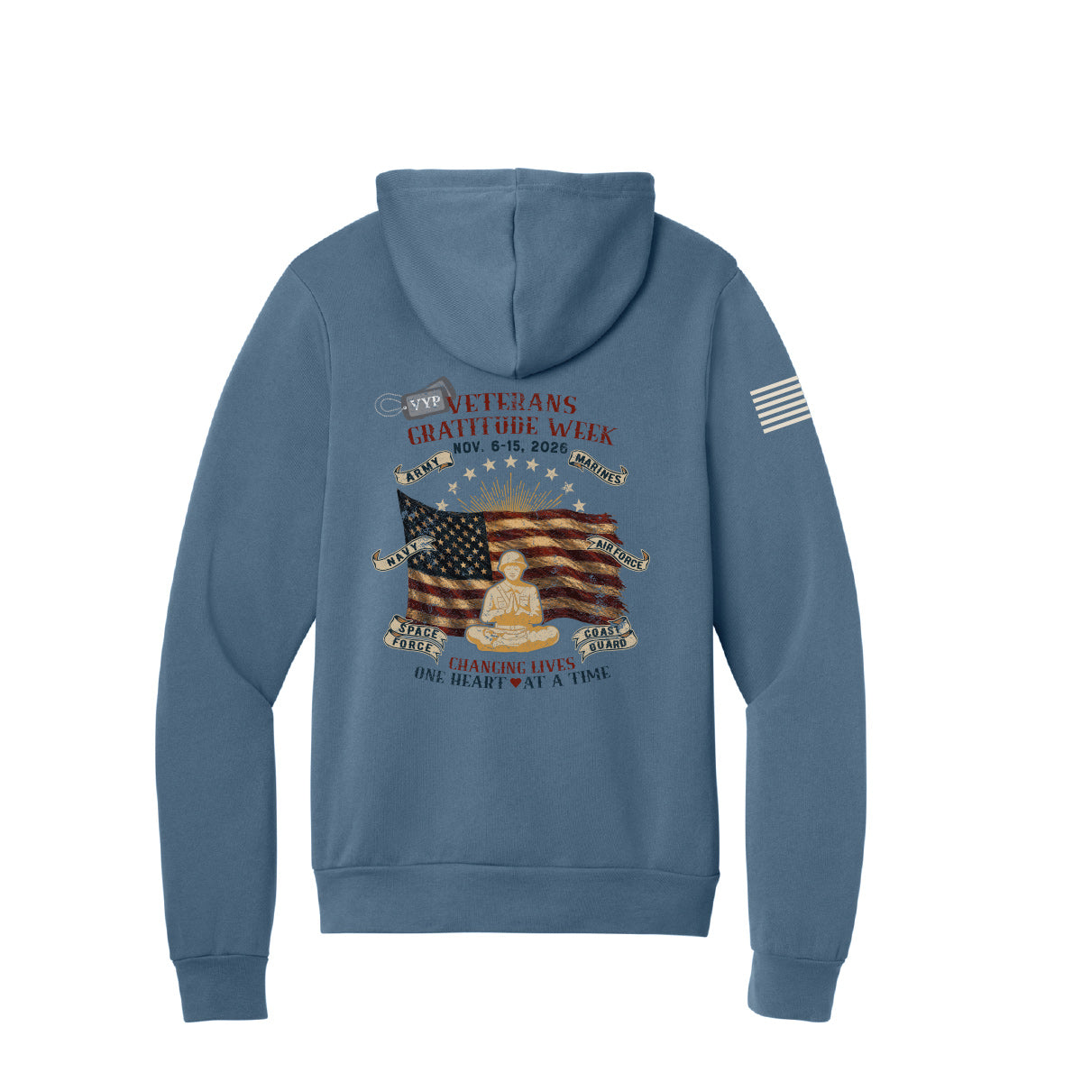 An indigo blue hooded sweatshirt shown from the back, featuring a large patriotic graphic with an American flag, a seated soldier, and text celebrating Veterans Gratitude Week. A charging American flag is printed on the right sleeve.